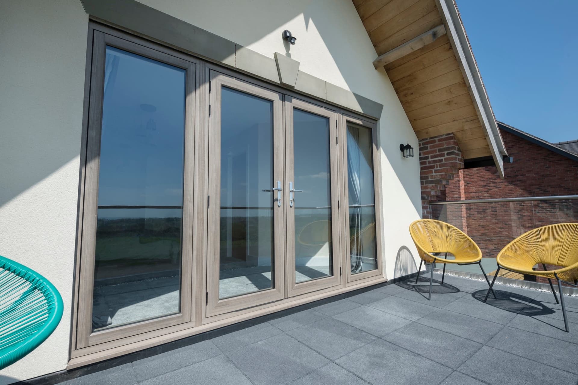 Schüco-quality aluminium bi-fold doors with woodgrain finish opening onto a sunlit patio