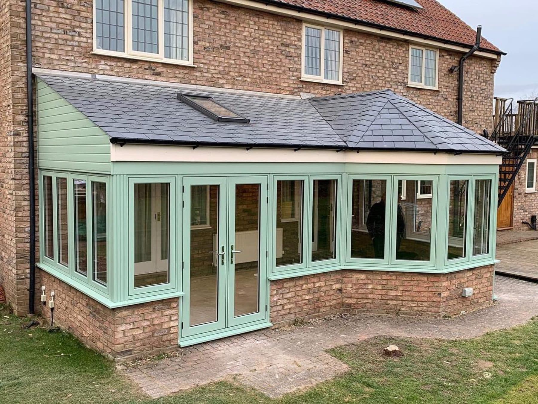 Sage green P-shape conservatory with Ultraframe roof on a Cambridgeshire brick home