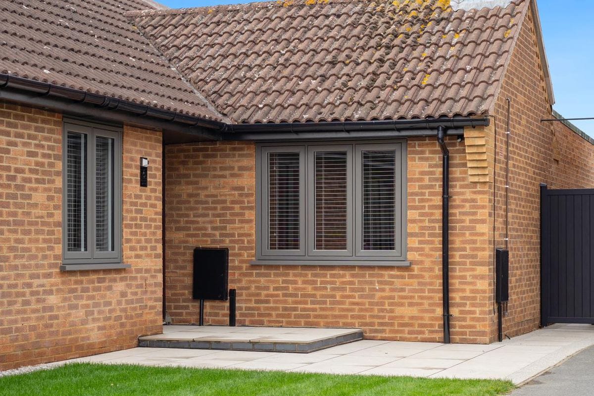 Anthracite UPVC casement windows with internal shutters on a red-brick bungalow