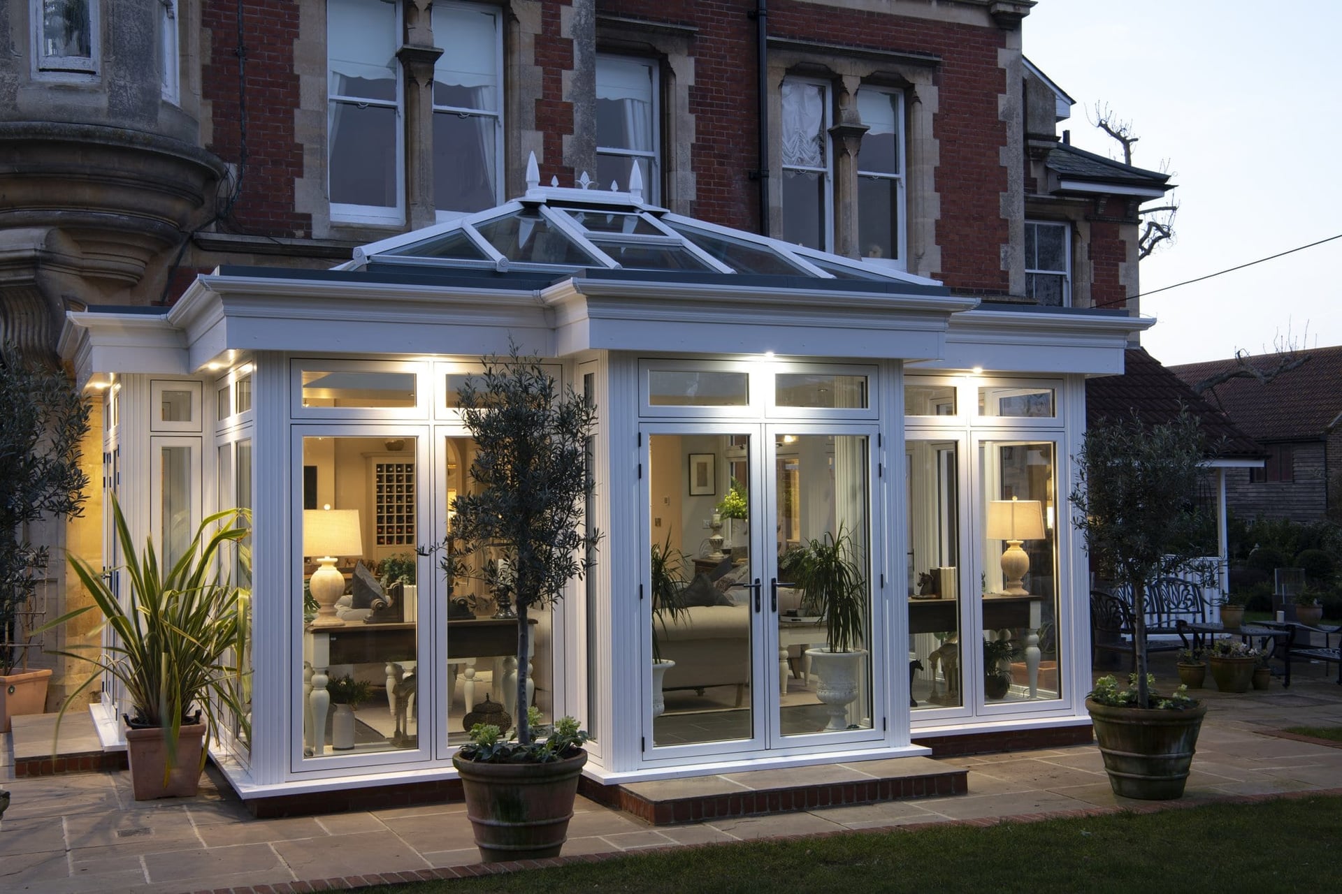 Period property with a contemporary orangery extension at dusk, warm interior lighting visible through Residence Collection bi-folding doors